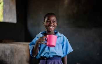 A girl smiles as she holds a pink mug of porridge